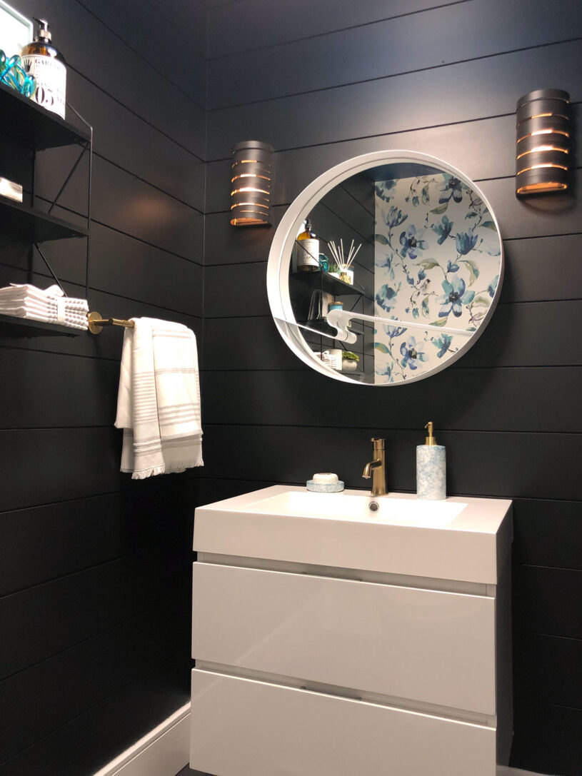 Our sleek and striking powder room reveal features black shiplap walls, a contrasting white vanity, bold patterned fabric wallpaper and gold accents